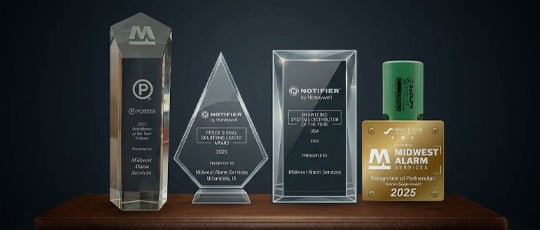 Four glass and metal corporate recognition awards from Potter and Notifier by Honeywell are displayed in a row on a wooden shelf against a dark background.